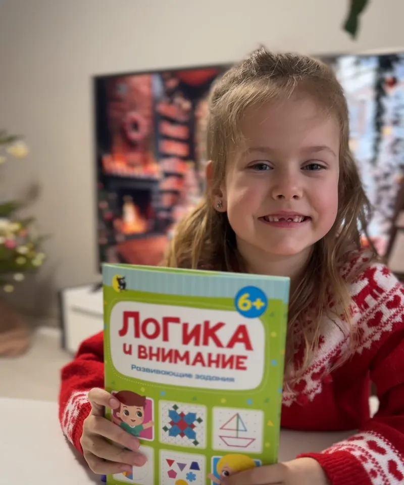 Девочка улыбается и держит тетрадь «Логика и внимание»